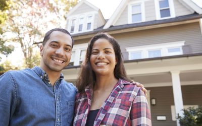 Smiling couple standing in front of their new home, illustrating the excitement of home ownership and mortgage success.