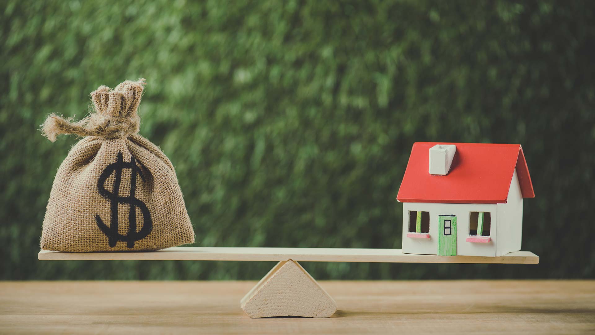 Money bag with dollar symbol balanced against a model house, symbolizing financial decisions in refinancing mortgages amidst economic uncertainty.